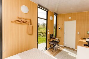 Una habitación moderna con paredes de madera, una cama, un escritorio con silla y vistas a un paisaje verde a través de un ventanal.