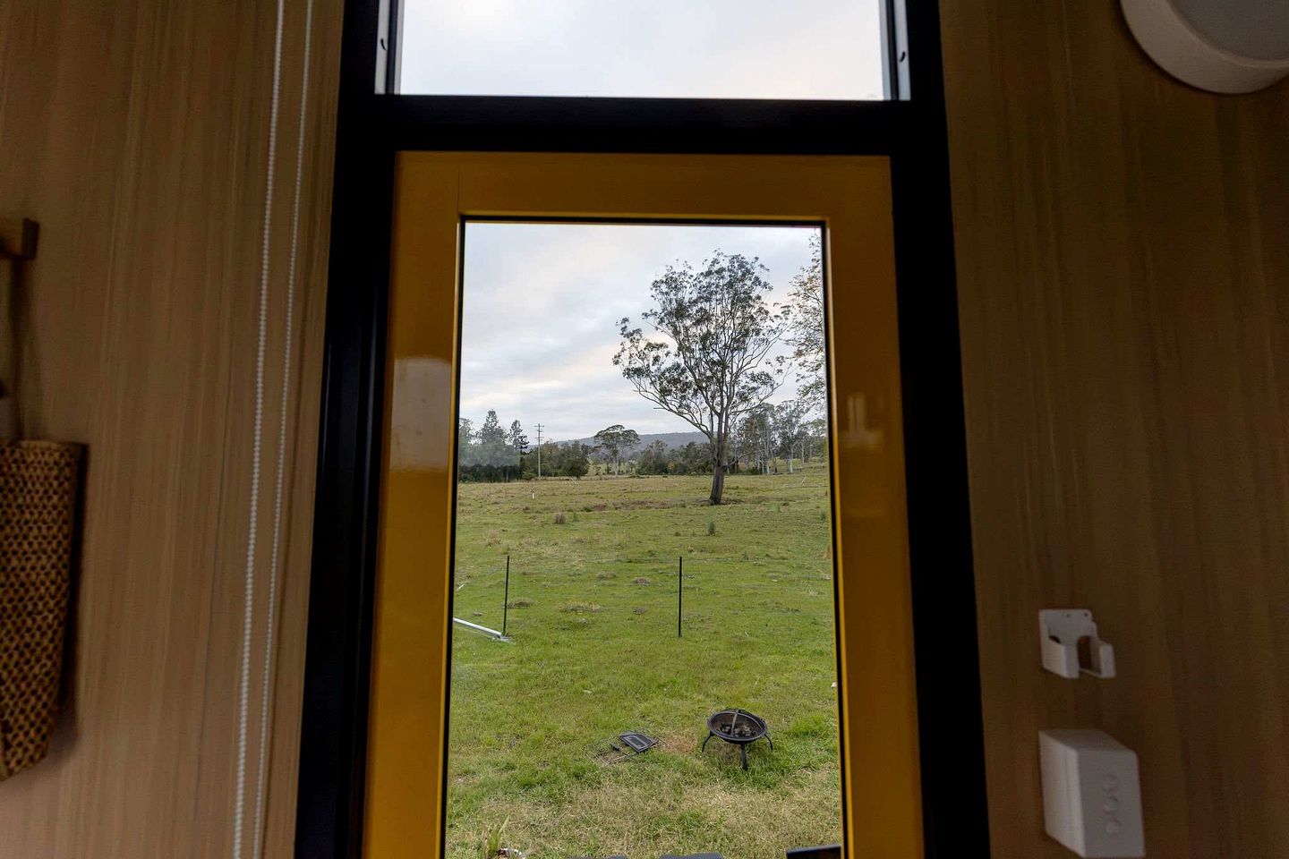 Eine Tür mit Blick auf eine grüne Außenanlage, einen Baum und eine Feuerstelle.