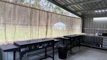 An outdoor kitchen area with two gas grills, a trash bin, and a metal table with a microwave.