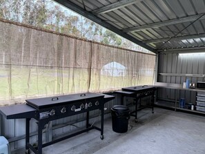 Zona cuina exterior amb dos grills de gas, un safata d'escombraries i una taula de metall amb microones.