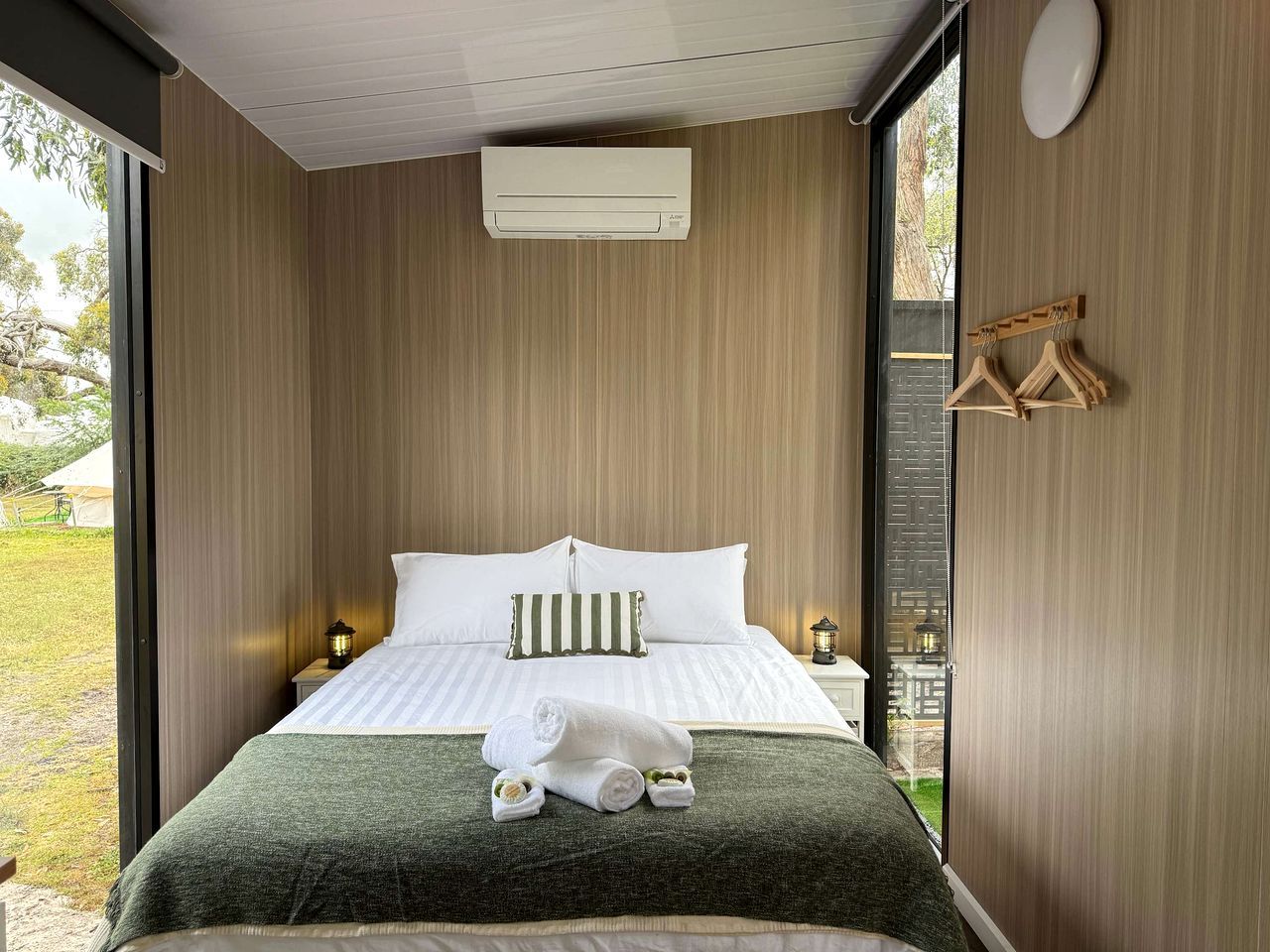 Een slaapkamer met een bed, kussens, een nachtkastje, een wandairconditioner en uitzicht op de omgeving.