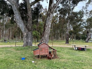 A wooden chicken coop in a grassy field with trees in the background.