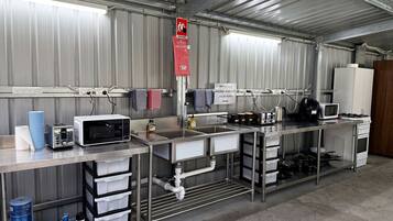 A commercial kitchen with stainless steel appliances, including a microwave, toaster, and sink. There are storage cabinets and a fire blanket sign.