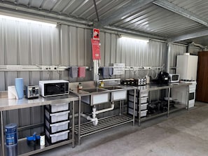 A commercial kitchen with stainless steel appliances, including a microwave, toaster, and sink. There are storage cabinets and a fire blanket sign.