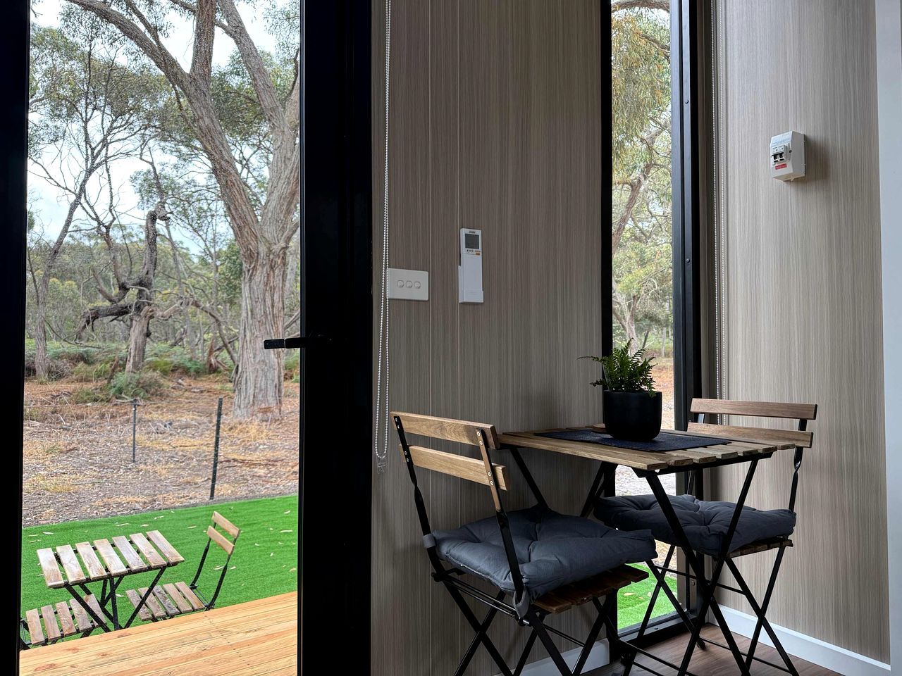 A room with a view of a garden, a table with chairs, and a potted plant.