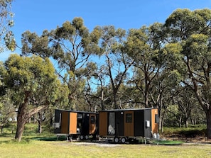 A modern, two-story mobile home with a flat roof, situated in a grassy area with trees in the background.