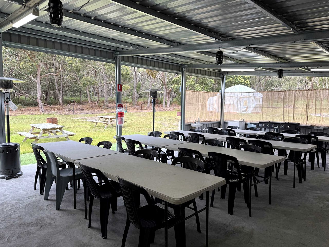 An outdoor covered dining area with tables and chairs, a trash can, and a view of the surrounding landscape.