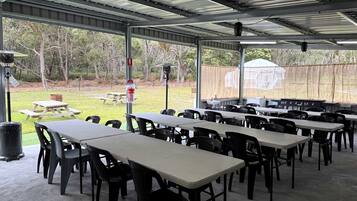 An outdoor covered dining area with tables and chairs, a trash can, and a view of the surrounding landscape.