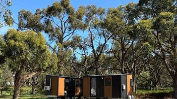 A modern, two-story mobile home with a flat roof, situated in a grassy area with trees in the background.