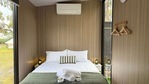 Quarto com cama, almofadas, mesa de cabeceira, ar condicionado fixado na parede e vista para o exterior.