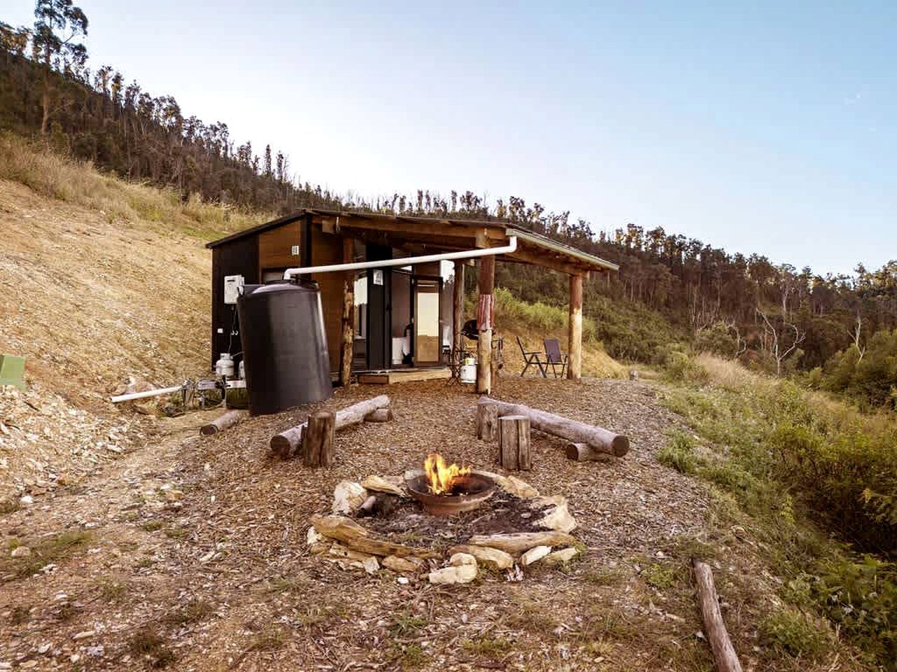 A rustic cabin with a fire pit, wooden deck, and a covered outdoor seating area.