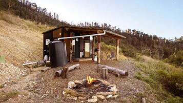 A rustic cabin with a fire pit, wooden deck, and a covered outdoor seating area.