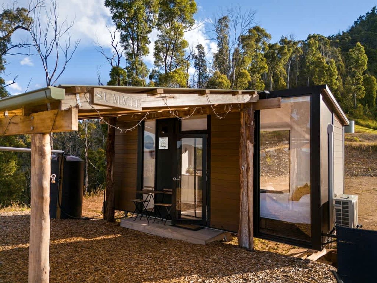 A small wooden structure with a covered entrance, a bench, and a table outside.