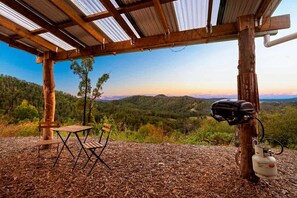 An outdoor seating area with a table and chairs, a grill, and a view of a forested landscape.