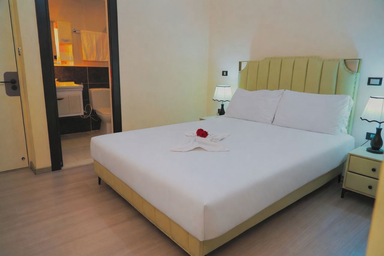 A hotel room with a bed, bedside lamps, a nightstand, and a bathroom visible through an open door.