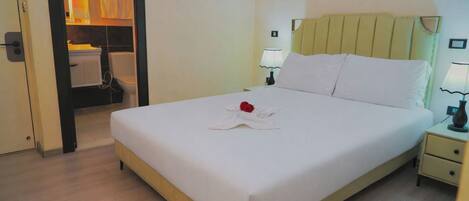 A hotel room with a bed, bedside lamps, a nightstand, and a bathroom visible through an open door.