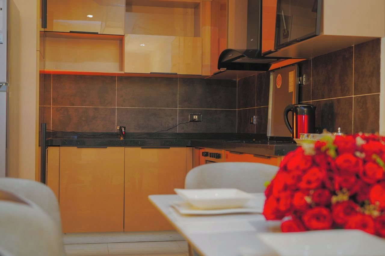 A modern kitchen with dark tiles, a coffee maker, and a table with a bouquet of red flowers.