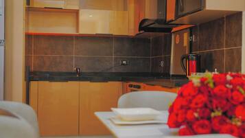 A modern kitchen with dark tiles, a coffee maker, and a table with a bouquet of red flowers.