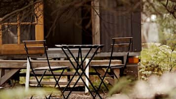 An outdoor wooden table and chairs set up in a natural setting with trees and foliage in the background.