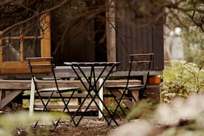 An outdoor wooden table and chairs set up in a natural setting with trees and foliage in the background.