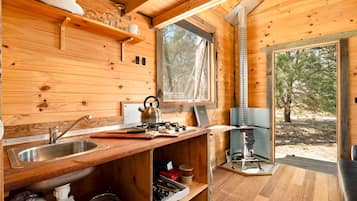 A wooden cabin interior with a kitchen area, including a sink, stove, and window.