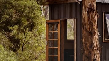 A small cabin with a wooden door and windows, surrounded by trees.