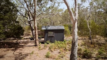 Une petite cabane à un seul étage, avec un toit en pente, entourée d’arbres dans une zone boisée.