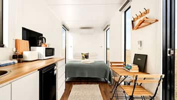 Een kleine kamer met een kitchenette, een bed, een bureau en een stoel.