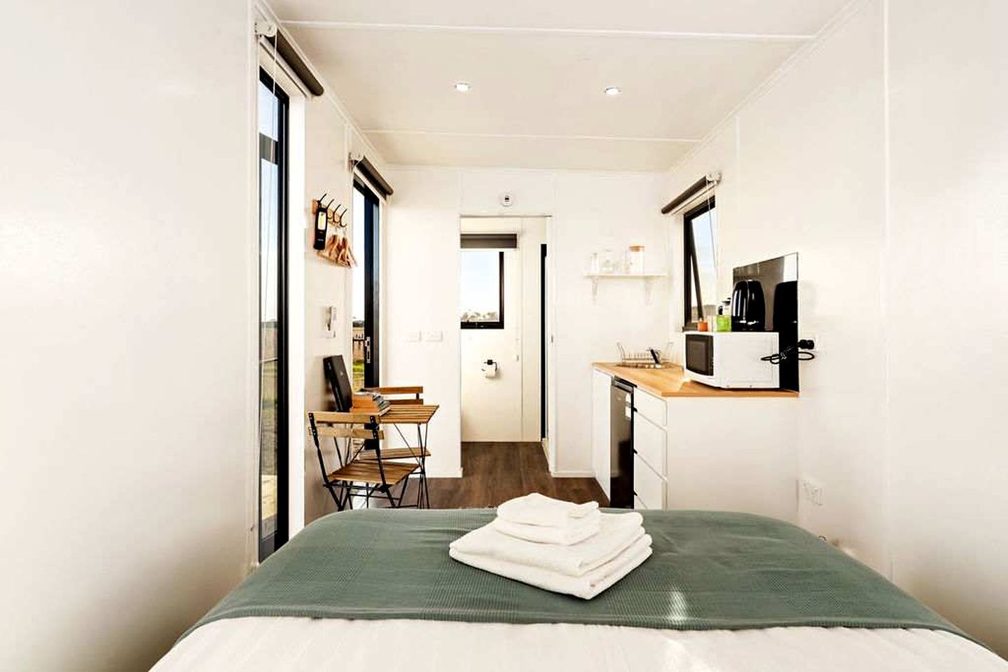A compact hotel room with a bed, a desk, a chair, a microwave, and a small kitchenette.