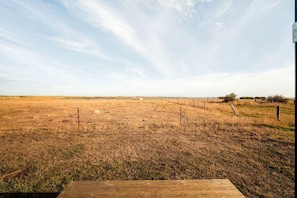 A flat, open field with a wooden deck in the foreground and a fence in the background.