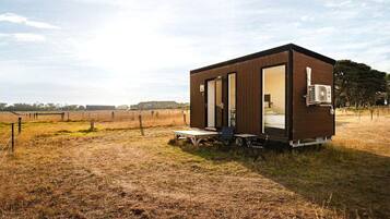 Un piccolo chalet con una stanza, una porta che dà su un'area notte, un tavolino e una sedia all'esterno.