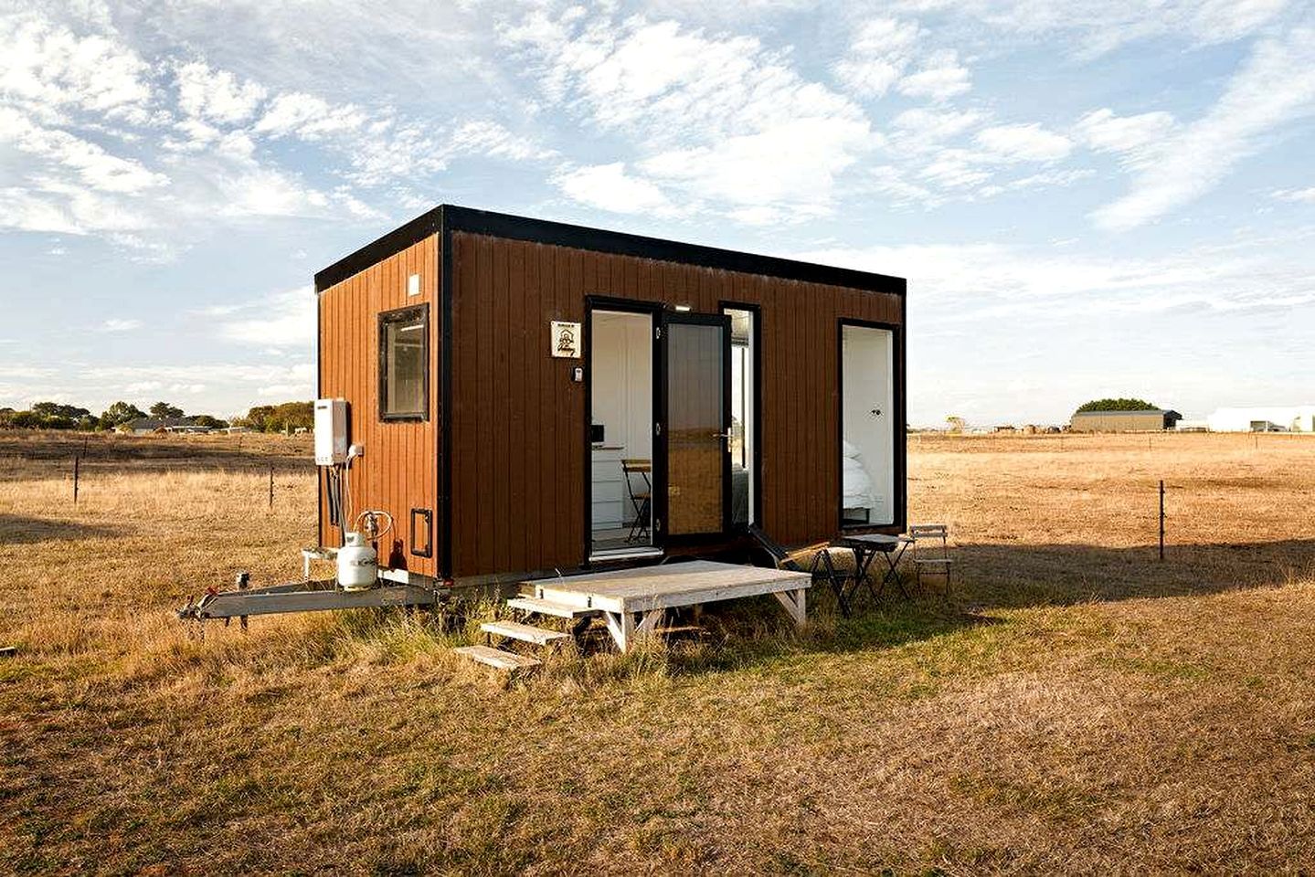Une petite cabane en bois avec une porte et des fenêtres, une table de pique-nique et un robinet d’eau à l’extérieur.
