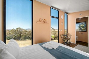 A bedroom with a large bed, a view of the outdoors, a small table, and a chair.