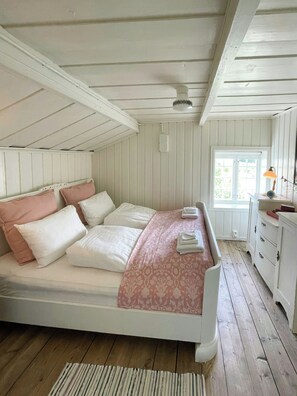 Ein Schlafzimmer mit einem Bett, Kissen, einem Nachttisch, einer Lampe und einem Fenster.