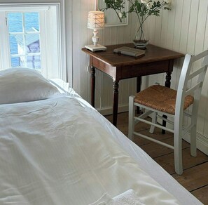 Een slaapkamer met een bed, een houten nachtkastje met een lamp, een stoel en een raam met uitzicht.