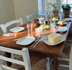 A wooden dining table set with plates, cutlery, a bottle of juice, a jar of honey, a glass of water, a bowl of fruit, and a block of butter. - **Historic Wooden House with Fjord Views (Råkvåg)