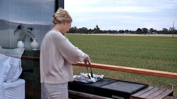 A person grilling outdoors with a view of a grassy field and trees in the background.