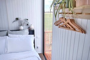 A bedroom with a bed, a nightstand, a potted plant, and a wooden hanger rack.