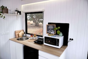 A compact kitchenette with a window, a sink, a microwave, and a small countertop area with various items.