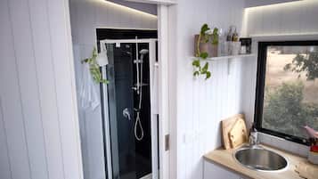 A modern bathroom with a glass-enclosed shower, a sink with a wooden countertop, and a window with a view of greenery.