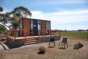 A modern cabin with a wooden deck, outdoor seating, and a view of the surrounding landscape.