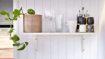 Uno scaffale bianco con una pianta in vaso, un bicchiere da vino, un bicchiere di vetro trasparente, una tazza bianca e saliera e pepiera.