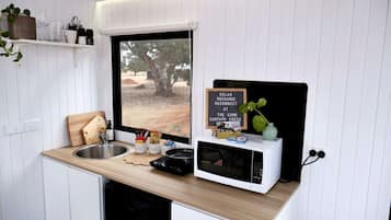 A compact kitchenette with a window, a sink, a microwave, and a small countertop area with various items.