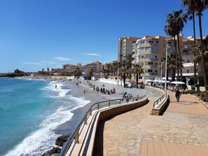 Eine Küstenpromenade mit gewundener Uferpromenade, Strand und Gebäuden im Hintergrund.