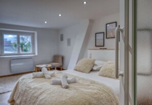 A bedroom with a bed, a chair, a small table, and a window.