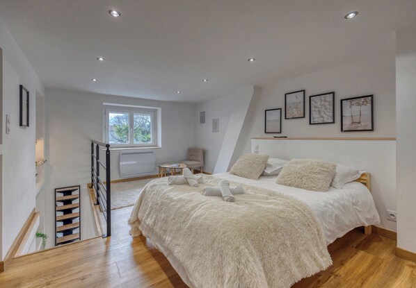 A bedroom with a bed, a chair, a window, and artwork on the wall.