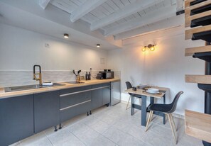 A modern kitchen with a central island, a dining area with a table and chairs, and a staircase with wooden steps.