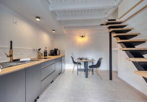 A modern kitchen with a central island, a dining area with a table and chairs, and a wooden staircase.