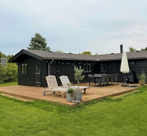 Eine Holzblockhütte mit einer Terrasse, ausgestattet mit zwei Liegestühlen, einem Tisch und einem Sonnenschirm.