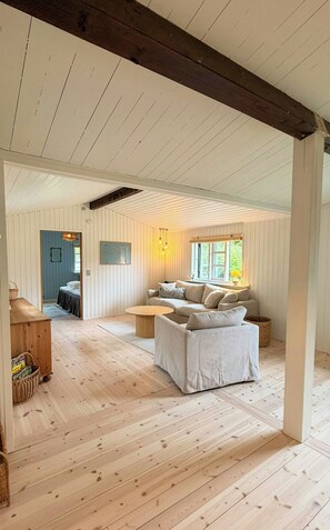 Een ruime kamer met houten vloer, een bank, een tafel en een raam met uitzicht.